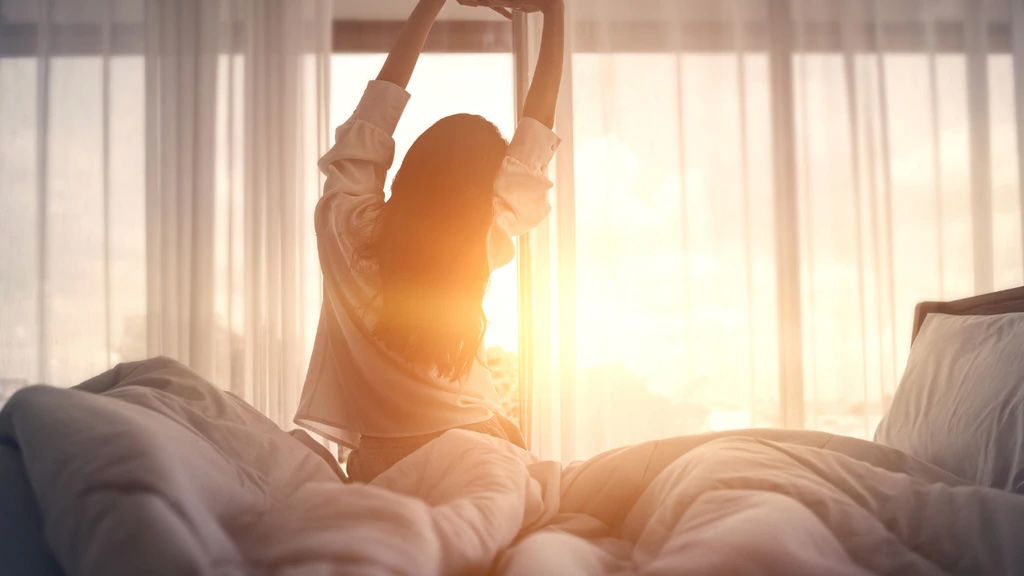 A woman standing in bed with her arms raised in the air.