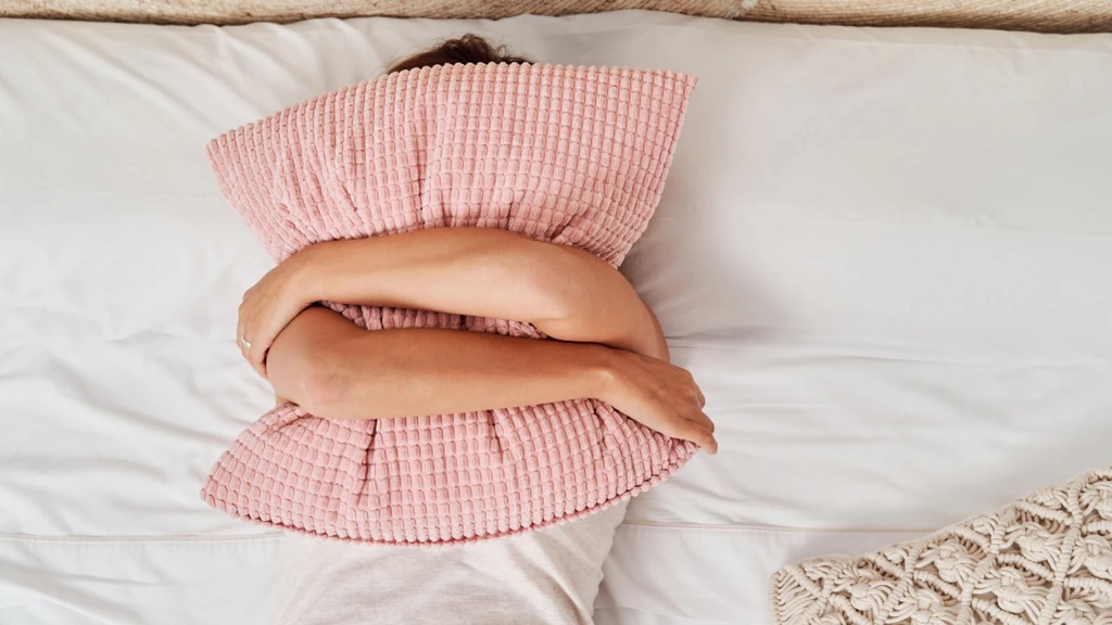 A woman peacefully sleeping on a bed with a pink pillow.
