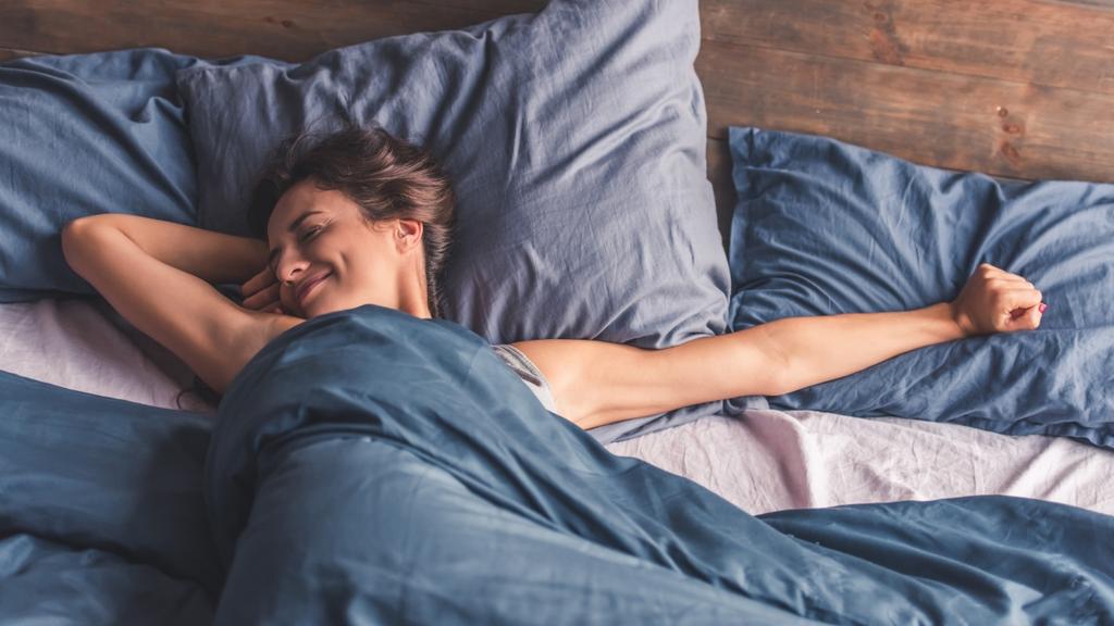 A woman peacefully sleeping in bed with blue sheets.