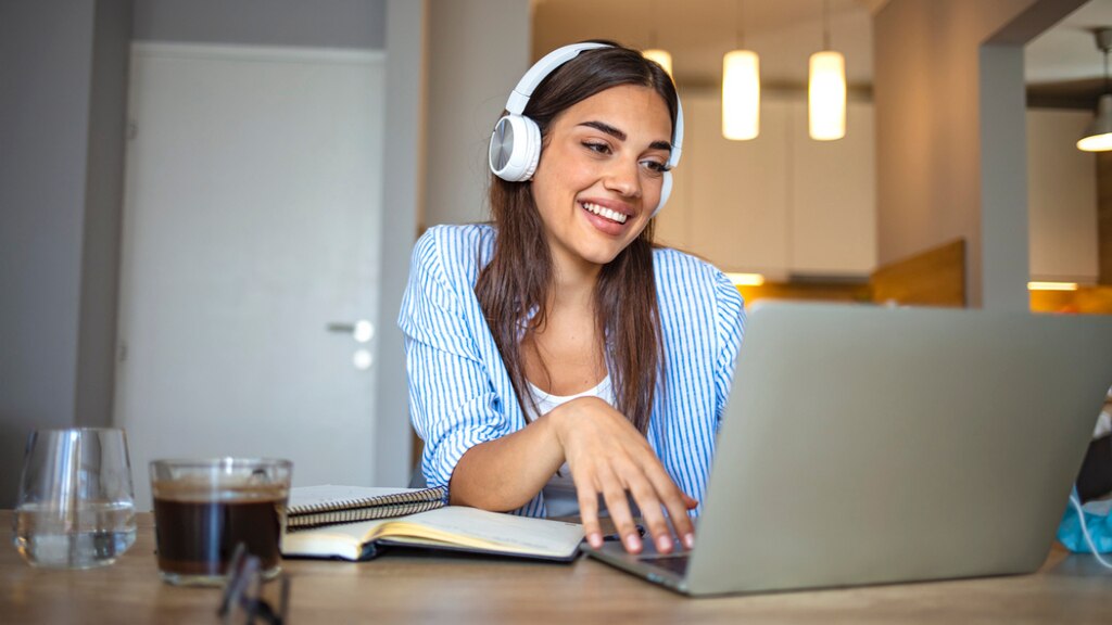 A smiling woman wearing headphones while using a laptop.