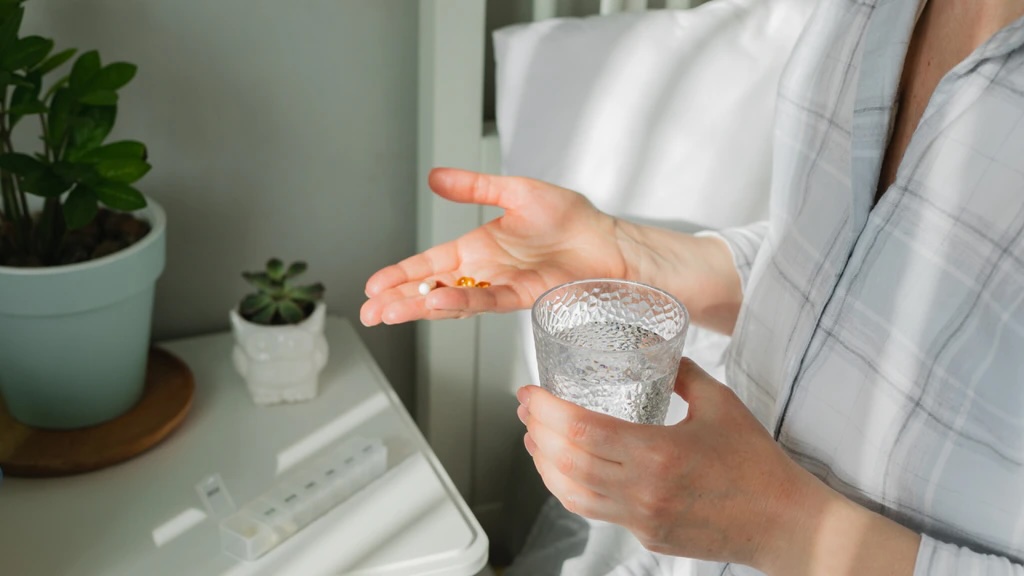 A woman holding a glass of water and a pill, ready to take medication for her health.